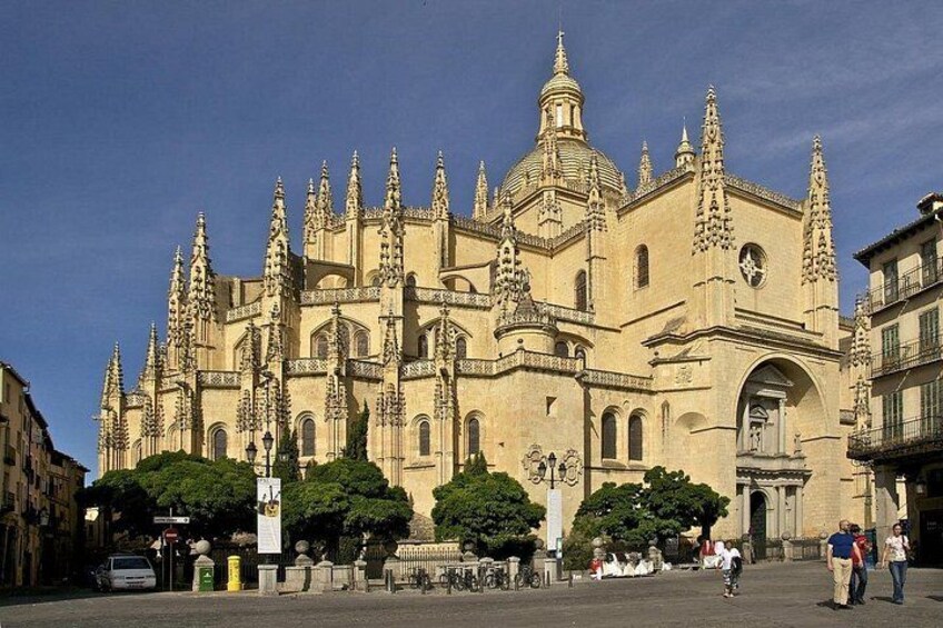 Une vaste cathédrale historique à l’architecture complexe, un ciel d’un bleu éclatant et quelques personnes se promenant au premier plan. 4