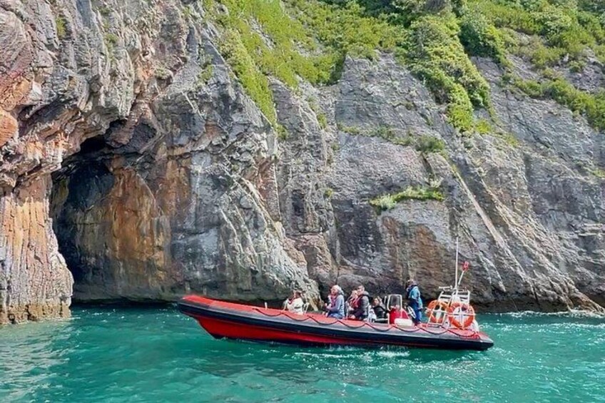 Un bote rojo con pasajeros cerca de la entrada de una cueva rocosa. 1