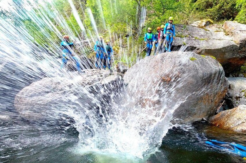 A waterfall with people standing on rocks, surrounded by greenery. 4