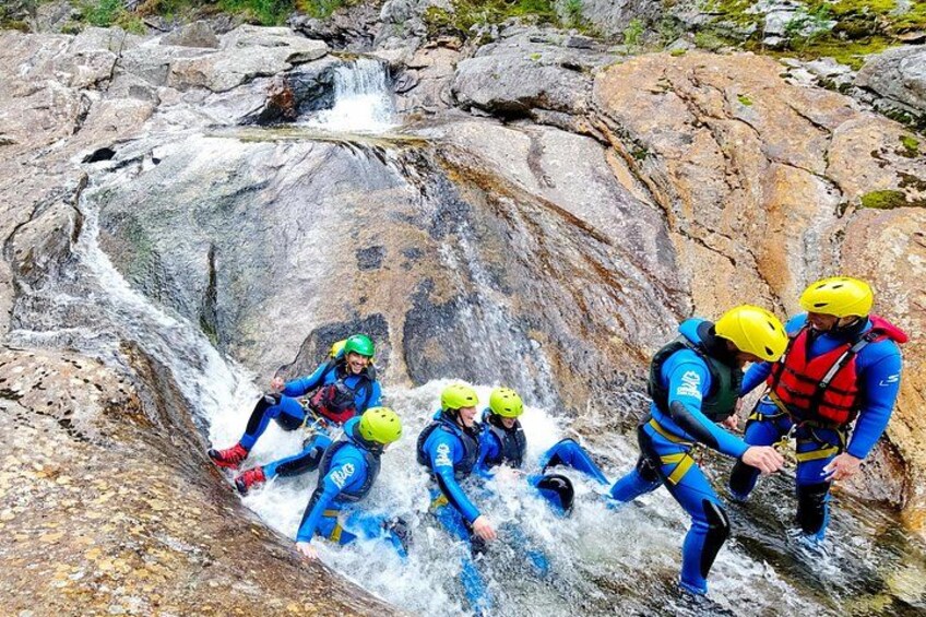 A group of people in blue and yellow wetsuits and helmets navigating a rocky watercourse. 5