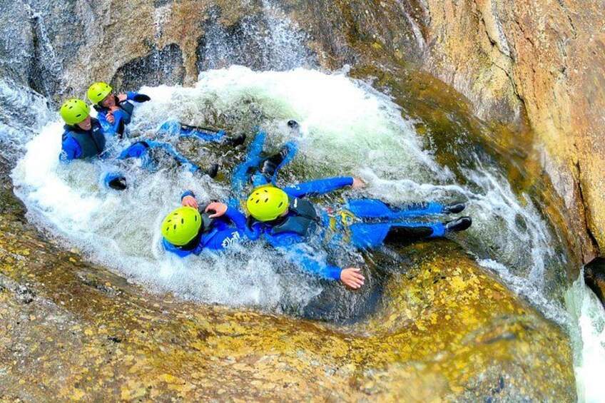 Un groupe de personnes, vêtues de combinaisons de plongée bleues et portant des casques jaunes, navigue sur un rapide en eaux vives à bord d’un radeau gonflable bleu. 3