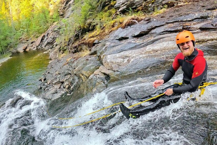 Une personne vêtue d’une combinaison de plongée rouge et noire et d’un casque orange, naviguant en kayak sur une rivière à courant rapide. 2