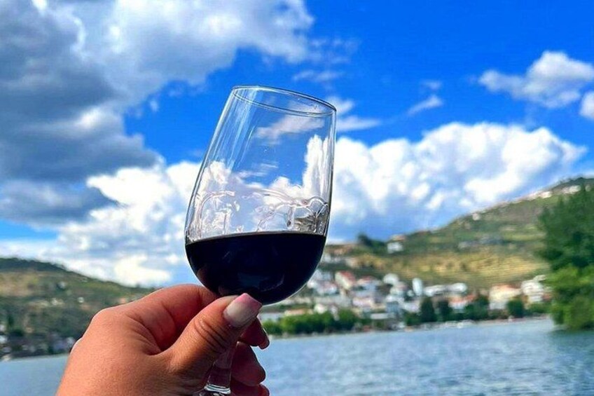 A hand holding a wine glass with a scenic view of a river and hills in the background. 1