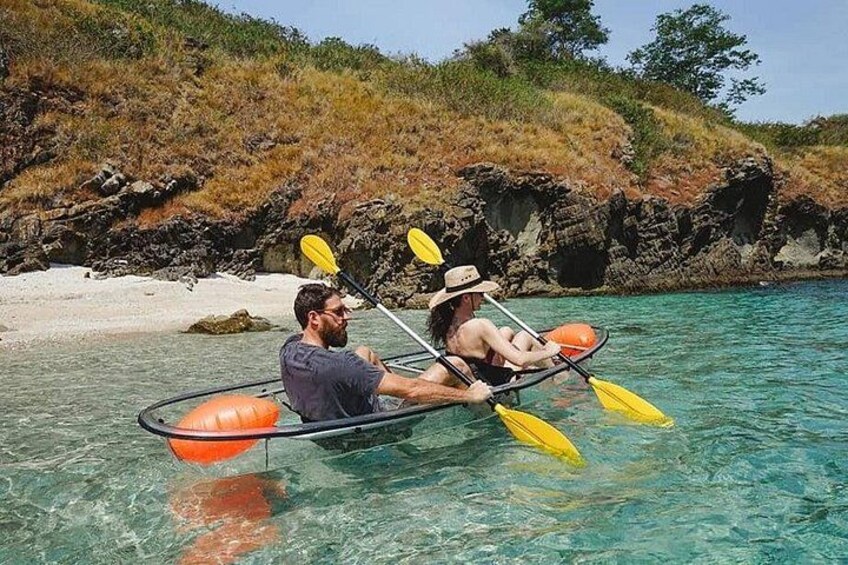 A couple kayaking on clear turquoise water with a rocky shoreline and sparse vegetation in the background. 2