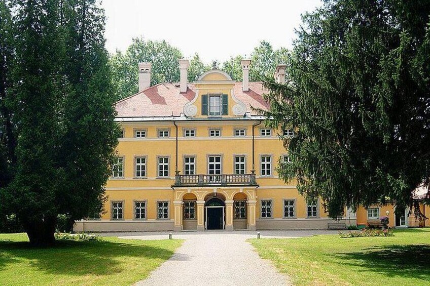Ein großes, gelbes Gebäude mit rotem Dach, umgeben von Bäumen und einem Kiesweg. 2