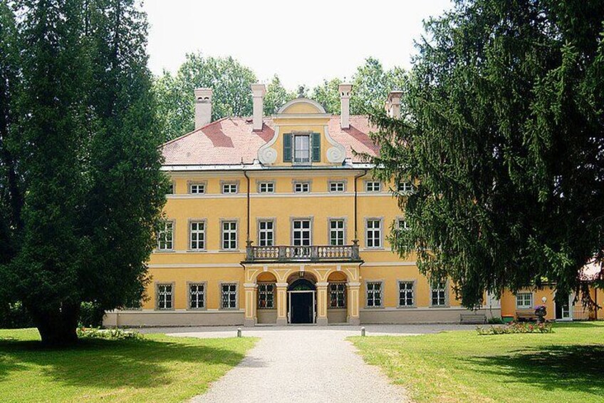 A large yellow building with a red roof, surrounded by trees and a gravel path. 3