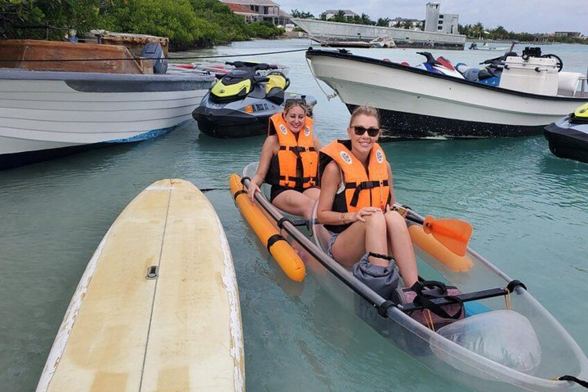 To personer i en lille båd med redningsveste, et surfbræt, og en jetski i baggrunden. 2