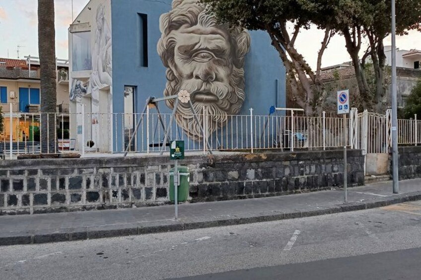 Une rue bordée d’un immeuble bleu orné d’une sculpture représentant la tête d’un lion, d’une clôture blanche et d’un panneau indiquant qu’il est interdit de se garer. 1