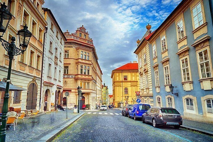 A cobblestone street lined with historic buildings, a blue car parked on the side, and a red car in the distance. 4