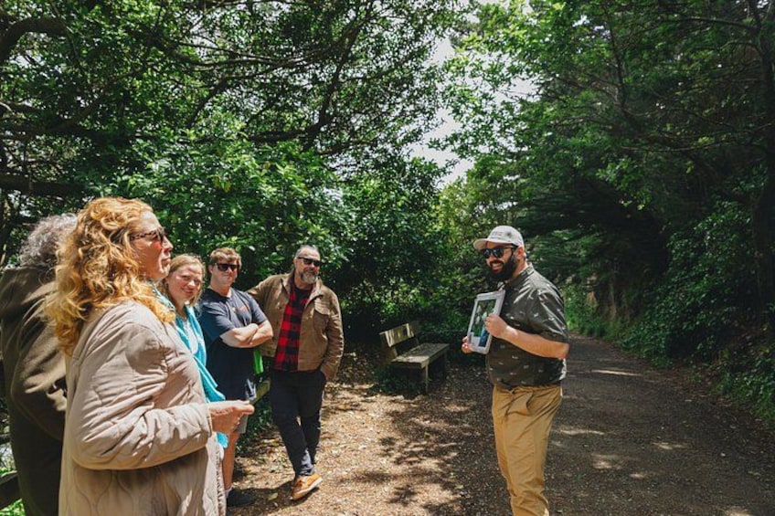 A group of people in a forested area with a dirt path, a bench, and a person holding a framed picture. 2
