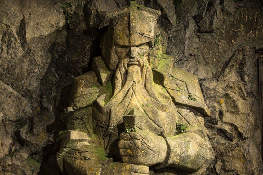 Una estatua de piedra de una figura con barba, rodeada de terreno rocoso. 1