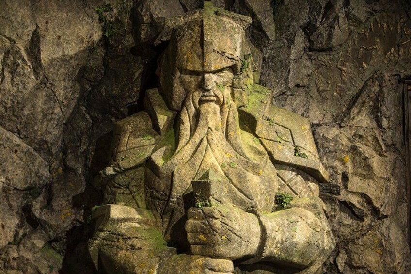 A large stone statue of a seated figure with a beard, set against a rocky background. 1