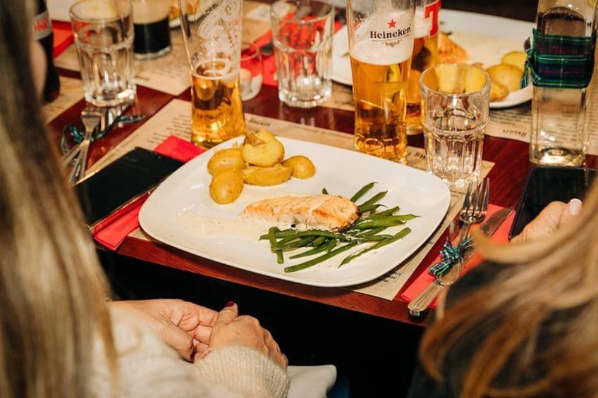 A dining table with a plate of food, glasses of beer, and a bottle of Heineken. 5