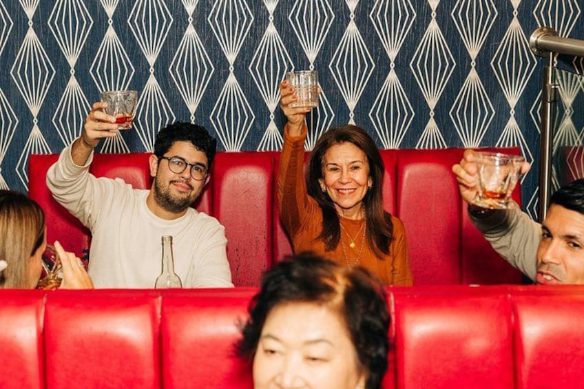 People seated on red upholstered booths with a patterned wall in the background. 3