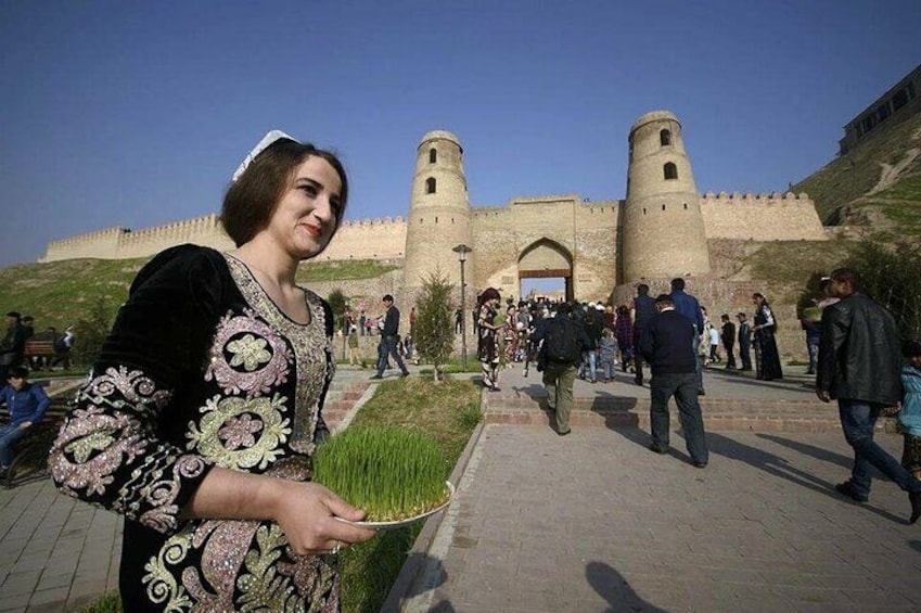 A person holding a tray of green plants in front of a historic fort with two towers. 1