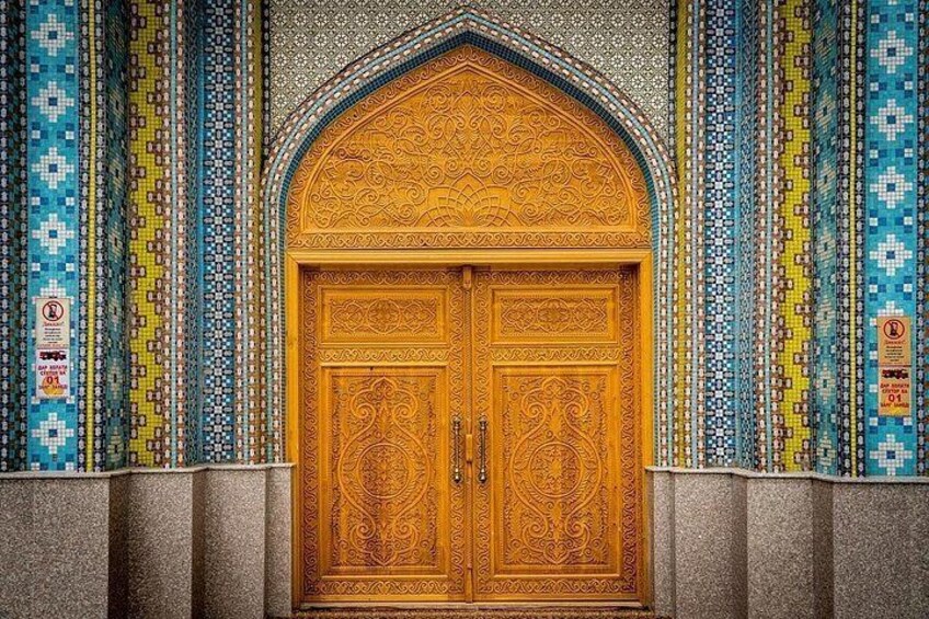 Une grande porte en bois, ornée de sculptures complexes, s’intègre dans un mur décoré de mosaïques colorées. 5