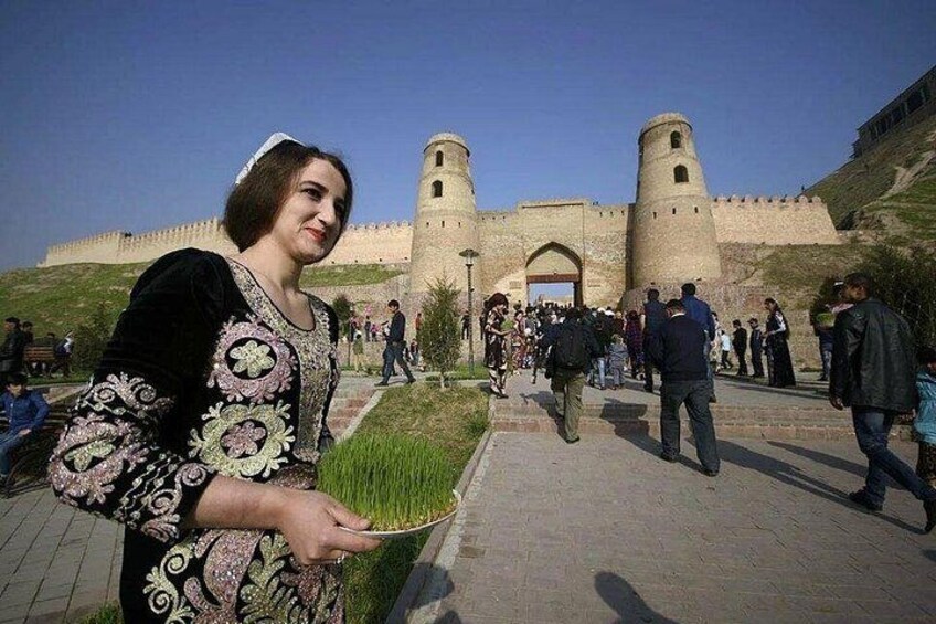 A person holding a plant, a historic fort with two towers, and a crowd of people. 1