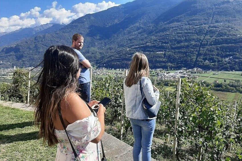 Three people standing on a grassy hill overlooking a valley with mountains in the background. 3
