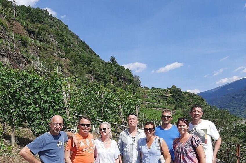 A group of people standing outdoors with a vineyard and hills in the background. 5
