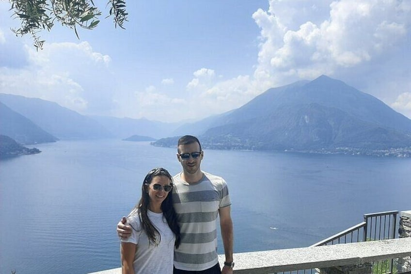 A couple standing by a lake with mountains in the background. 2