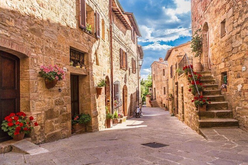Una stretta via in pietra fiancheggiata da edifici tradizionali, con fioriere e uno scooter parcheggiato a lato. 3