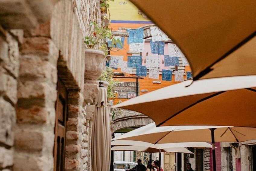 A narrow alley with brick walls and outdoor seating under umbrellas. 2