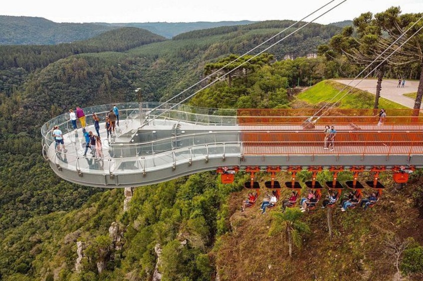 A glass bridge with people walking on it, surrounded by a forested landscape. 2