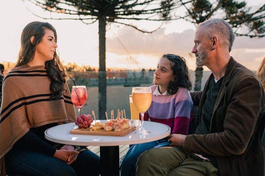 A group of people sitting at a round table outdoors with drinks and snacks. 3