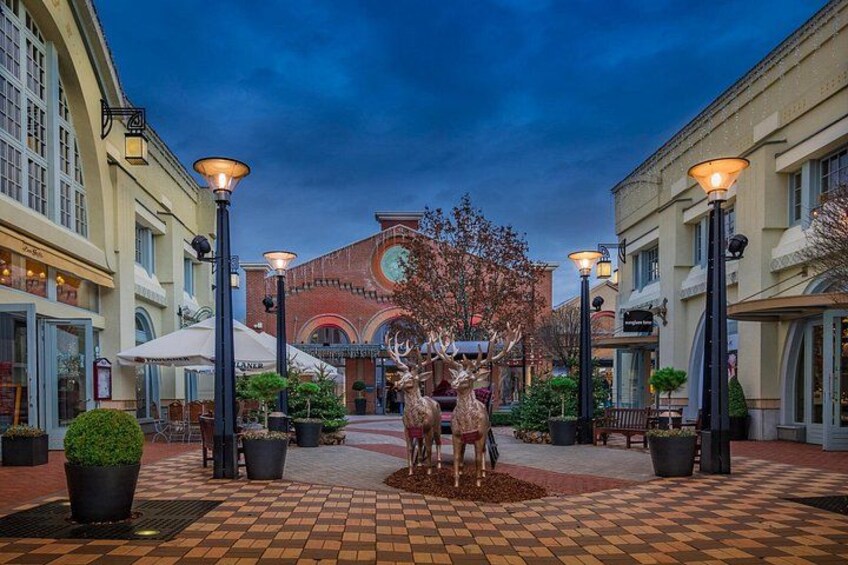 A plaza with a decorative deer sculpture, potted plants, and a building with a clock in the background. 3
