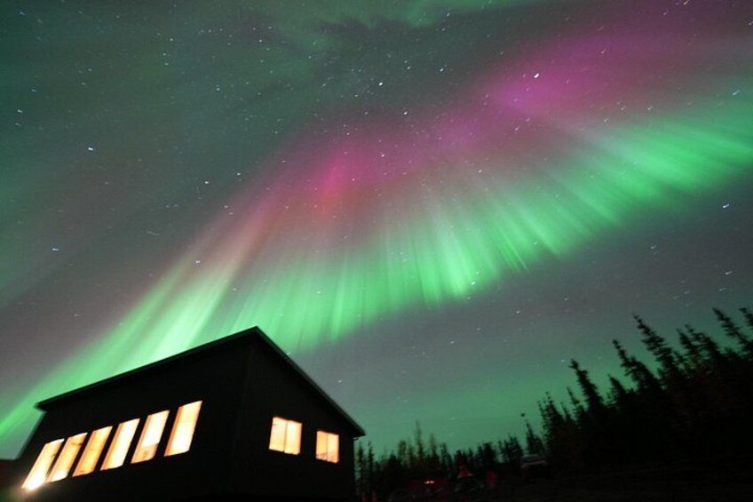 A house with illuminated windows under a night sky with green aurora borealis. 4