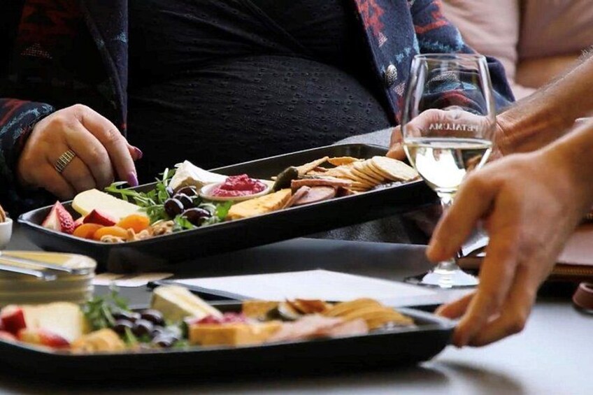 Eine Person serviert Speisen von einem Tablett, darunter Käse, Obst und Gemüse. 3