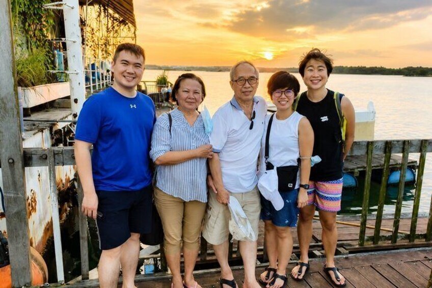 A group of people standing on a wooden dock by a body of water during sunset. 4