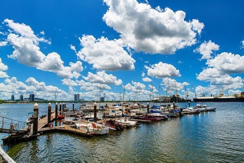 A marina with boats docked, a clear blue sky, and distant city buildings. 2