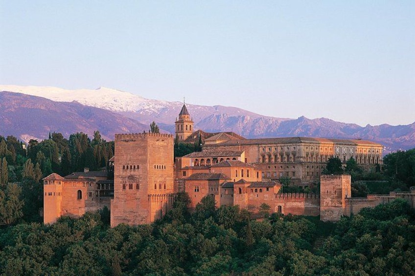 A historic castle complex with towers and a large building, surrounded by trees and mountains in the background. 2