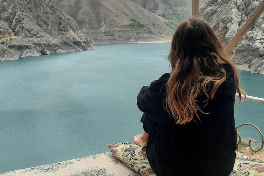 A person sitting by a calm blue lake with rocky cliffs in the background. 5