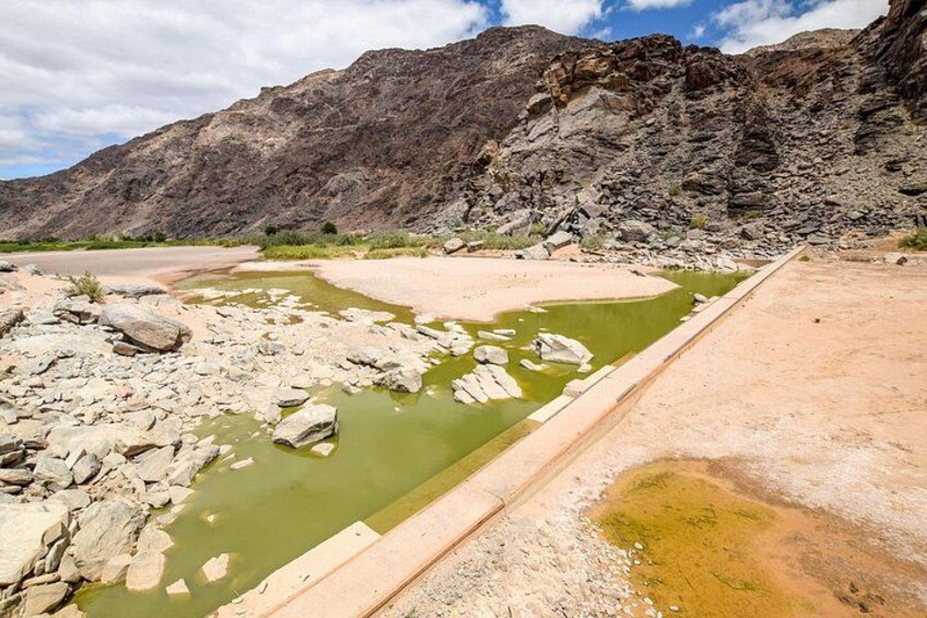 A dry riverbed with scattered rocks and a small body of water. 4