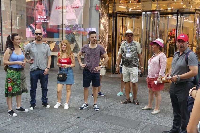 A group of people standing on a sidewalk in front of a store with glass doors. 2