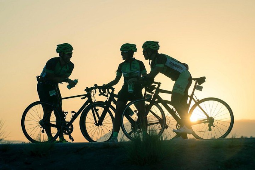 Tre cyklister på en väg i solnedgången. 1