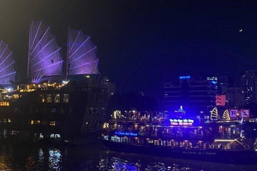 A nighttime view of a river with illuminated buildings and a large ship with sails. 4