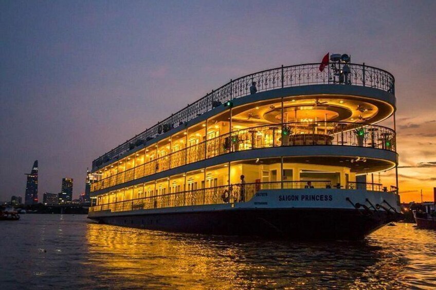 A large, multi-deck riverboat named 'Saigon Princess' with a circular design, illuminated by warm lights against a twilight sky. 1