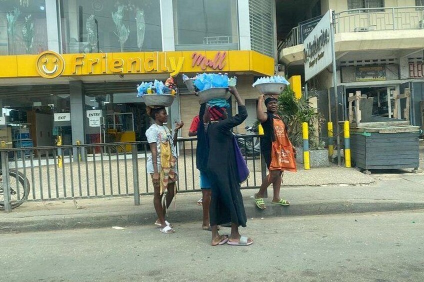 Tre persone che trasportano oggetti in testa davanti a un edificio con un cartello giallo che riporta la scritta 'Friendly Mall'. 5