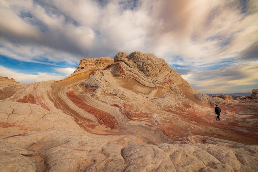 A desert landscape with layered rock formations and a person walking. 1