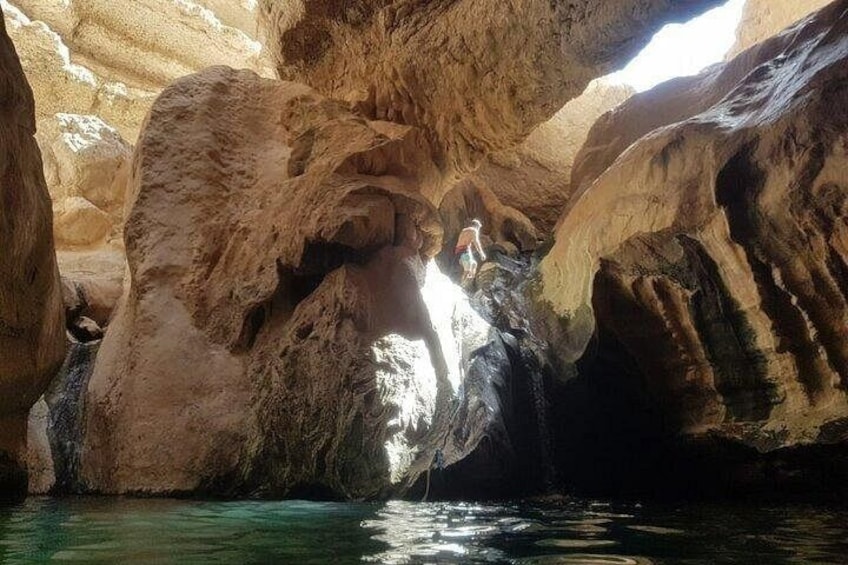 Una cueva con estalactitas y estalagmitas, agua que fluye por el interior, y una persona de pie sobre una roca. 4