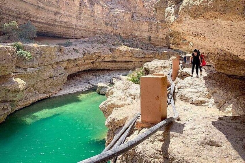 Un cañón con una piscina turquesa, terreno rocoso y una barandilla de madera. 2
