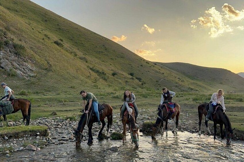 A group of people riding horses along a rocky stream in a hilly landscape. 3