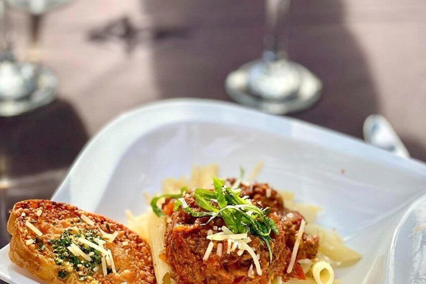 Plato con pasta, una rebanada de pan y un guiso de carne, posiblemente un filete, adornado con hierbas. 3