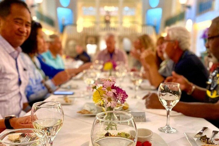Una mesa de comedor con copas de vino, platos y un jarrón de flores. 1