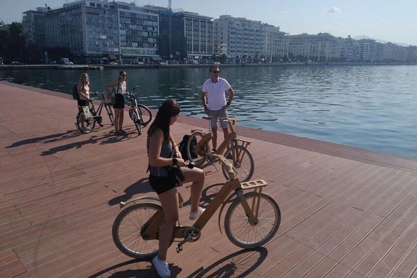 Ein hölzerner Steg entlang eines Gewässers, mit Menschen und Fahrrädern. 3
