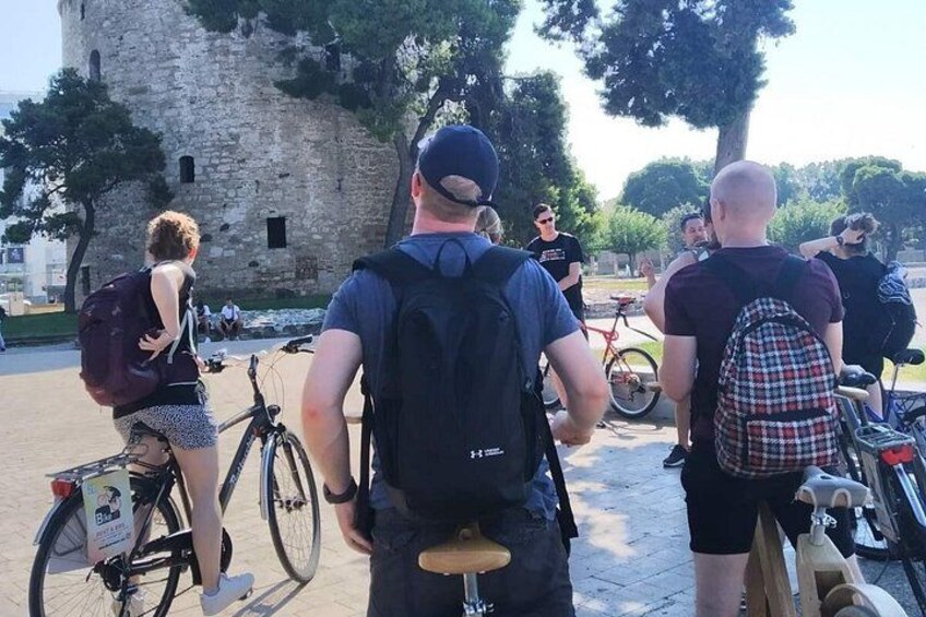 Eine Gruppe von Menschen mit Fahrrädern und Rucksäcken in der Nähe eines historischen Steinturms. 4