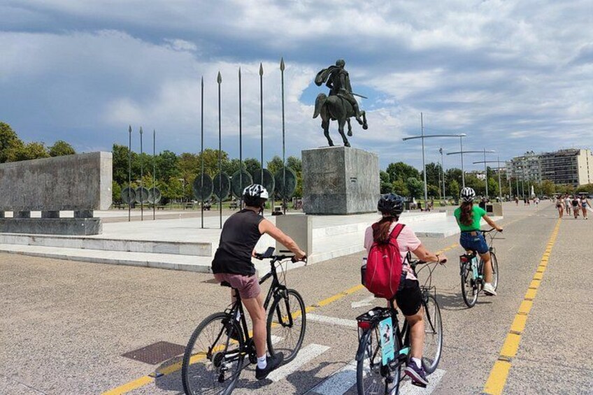 Tres ciclistas en un camino pavimentado con una estatua al fondo. 1